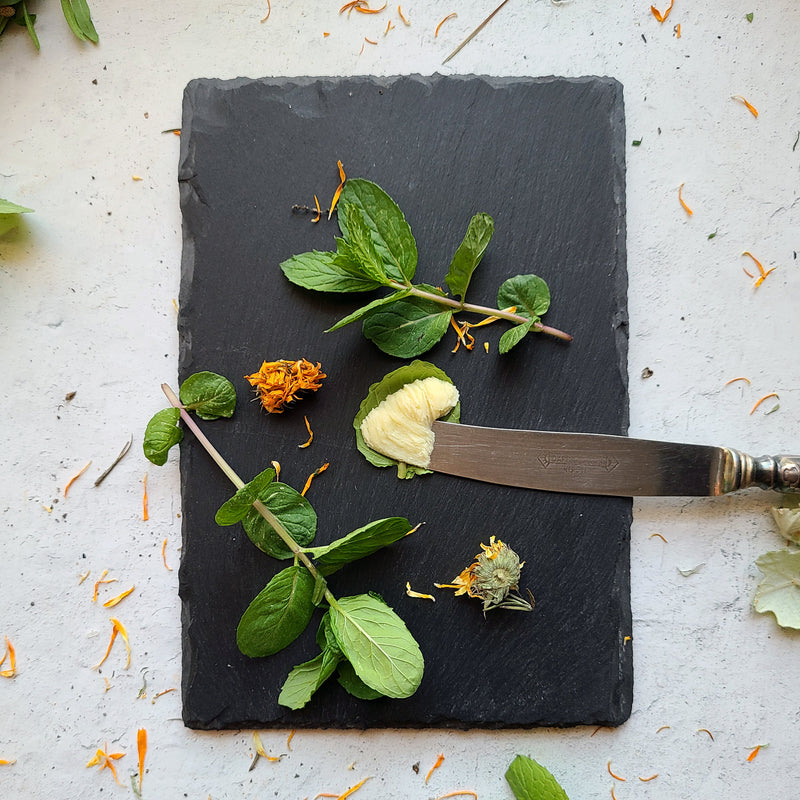 Hand and Foot Rescue Salve on butter knife with fresh mint and dried calendula flowers