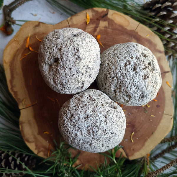 3 light colored pumice stones on cedar stump encircled with pine branches